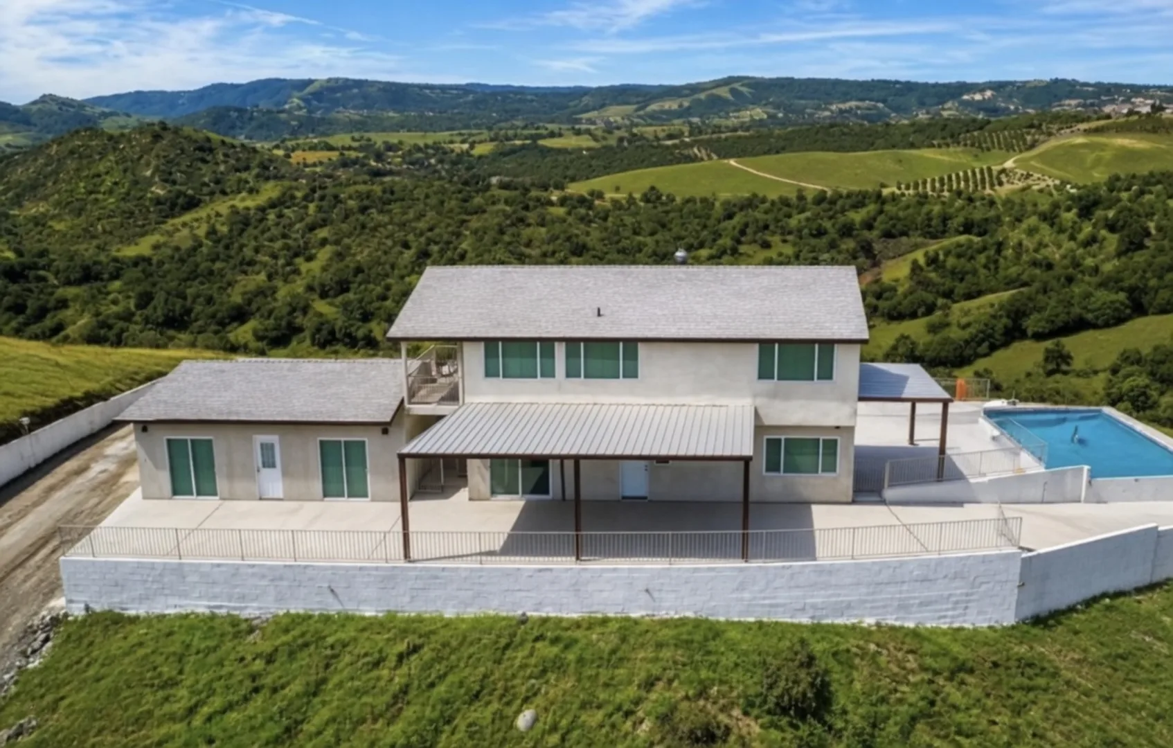 A two-story Temecula hilltop estate with a backyard pool, retaining wall, and panoramic views of rolling green hills and distant mountains